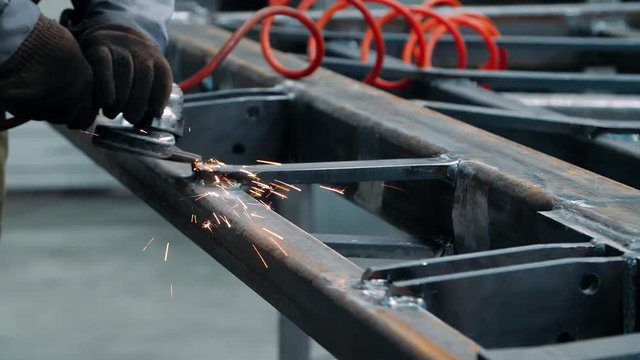 Man working with electric wheel grinding on steel structure at factory