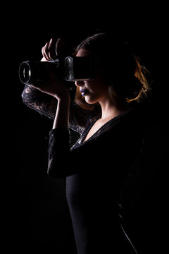 Asian Woman Photographer hold camera with external flash point to shoot subject, wear body suit. studio lighting black background isolated low key exposure, reporter journalist take photo celebrity