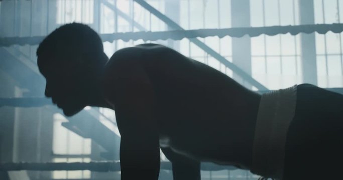 Cinematic slow motion shot of a professional young muscular shirtless african man is practicing shadow boxing work out in a ring. 