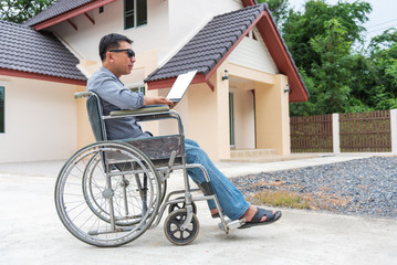 Fototapeta na wymiar Disabled middle-age Asian person in the wheelchair work at home with laptop.