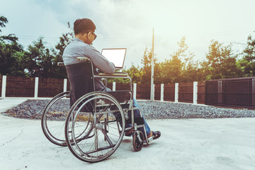 Disabled middle-age Asian person in the wheelchair work at home with laptop.