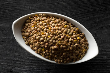 Raw, dry, uncooked brown lentil legumes in white bowl on wood table background top view flat lay from above