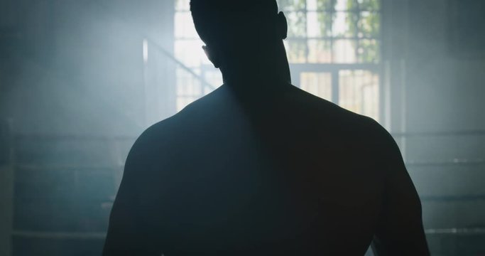Cinematic slow motion back view shot of a professional young muscular shirtless african man is practicing shadow boxing work out in a ring. 