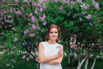 Charming woman wearing beautiful white dress standing next to lilac bush. Copy space.