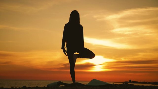 Silhouette young woman practicing yoga at sunset on the sea. Happy moments of life - silhouette yoga on the beach on the sunset. Fitness and healthy lifestyle.
