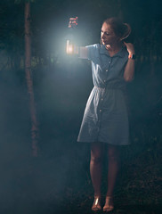 Beautiful girl in denim dress in misty forest with lantern in hand