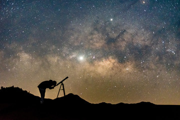 Silhouette of man watching star in telescope against  milky way galaxy with stars and space dust in...