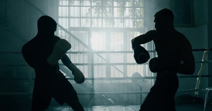 Cinematic slow motion shot of two professional young muscular shirtless male boxers are fighting  in a boxing ring.