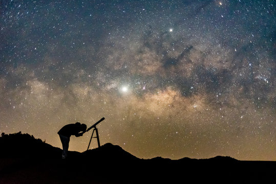 Silhouette of man watching star in telescope against  milky way galaxy with stars and space dust in the universe.
