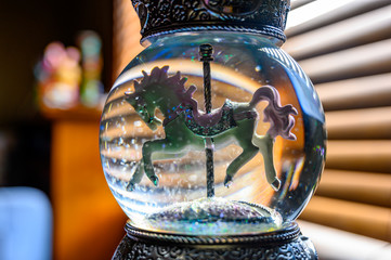 Glitter snow globe with carousel horse.  Window blinds in background