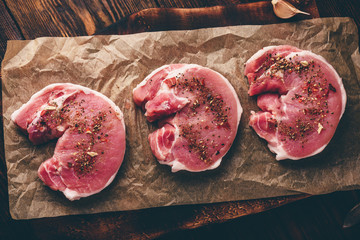 Raw pork loin steaks with different spices on baking paper