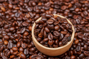 Wooden bowl with roasted coffee beans on rustic background.