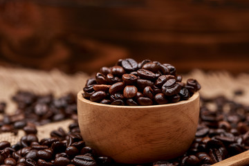 Wooden bowl with roasted coffee beans on rustic background.