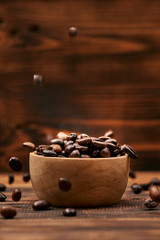 Wooden bowl with roasted coffee beans on rustic background.