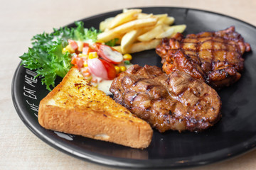 The roasted pork with buttered bread and french fried and vegetable in the dark plate in the natural light. 