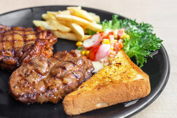 The roasted pork with buttered bread and french fried and vegetable in the dark plate in the natural light. 
