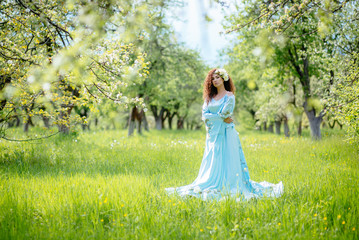 Beautiful girl is standing in the spring apple garden in a long dress