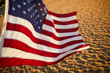 Close-up of American flag with stripes and stars blowing in wind on summer beach at sunset
