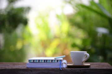 White coffee cup and diary notebooks with pencil on brown wooden table at outdoor