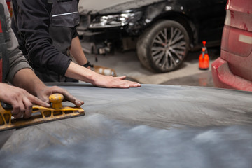 Preparation for painting a car element using emery sender by a service technician leveling out before applying a primer after damage to a part of the body in an accident in the vehicle workshop