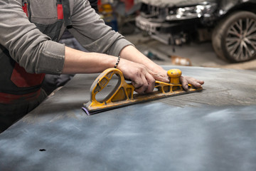 Man worker preparing for painting a car element using emery sender by a service technician leveling...