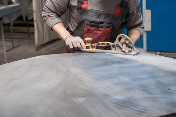 Preparation for painting a car element using emery sender by a service technician leveling out before applying a primer after damage to a part of the body in an accident in the vehicle workshop