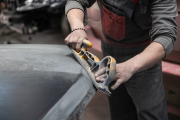 Preparation for painting a car element using emery sender by a service technician leveling out...