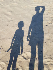 Shadow of father and son standing side by side on the sea shore.