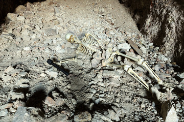 Skeleton in a dark cave in the ground lying on rocks