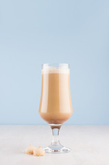 Irish coffee with cream and biscuits in transparent wineglass on white wood board in light blue color background, copy space, vertical.