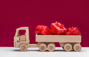 Truck with gifts in red boxes. Wooden toy car. Red background, copy space, holiday concept. - Powered by Adobe