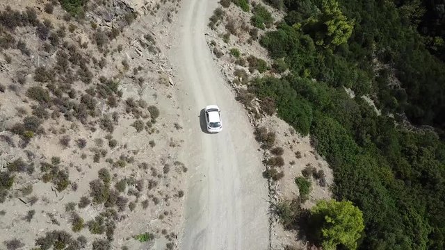 Top down tracking shot white car driving down mountain road, Greece