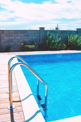 Swimming pool with stair at hotel. Sunny reflections.