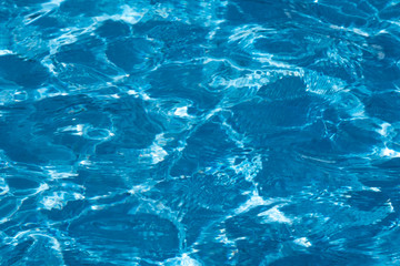 Blue and bright ripple water surface in swimming pool with sun reflection.