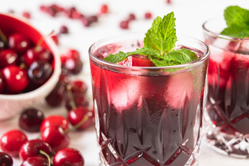 Fresh Cherry Juice in Glasses With Mint Leaves and Ice Cubes, and Fresh Cherries on a Table Close Up on White Background