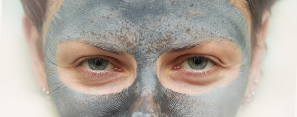 Fototapeta premium Skin care. Woman face with cosmetic spa clay mask closeup. Girl model with grey mask doing beauty spa treatment