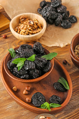 Bowl and plate with tasty prunes on wooden table