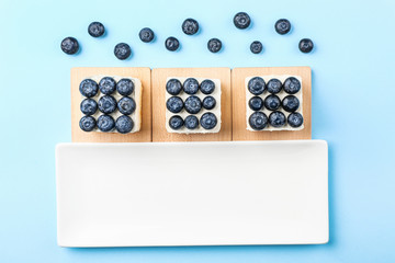 Tasty blueberry cakes on color background
