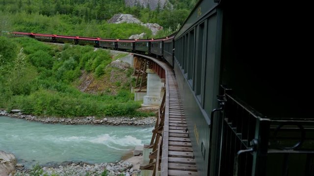 A train crosses a river on a wooden bridge while traveling through Alaska.
