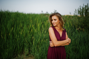 Blonde sensual woman in red marsala dress posing in the reeds.