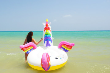 Young woman swimming with unicorn in Mediterranean sea in vacation. Guardamar, Spain