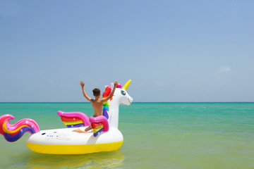 Happy little boy swimming with unicorn in waves on beach of Mediterranean sea. Guardamar, Spain