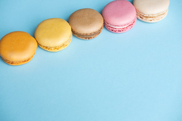 Top view of tasty colorful macaroons on blue background with place for text