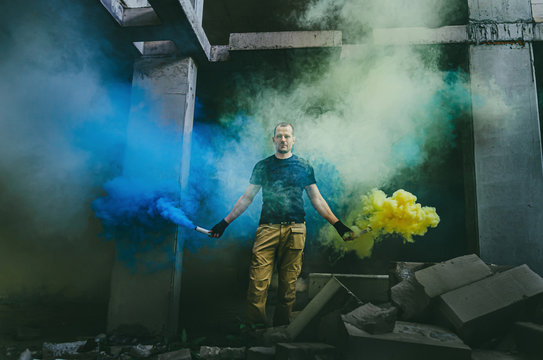 Attractive sporty man in an abandoned building holding colored smoke - blue and yellow.