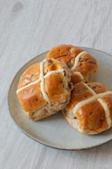 Hot cross buns piled on a green glazed plate with a grey wood background