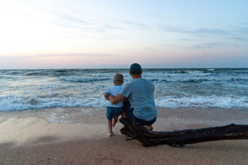 father and son watch the sea from the shore in the evening