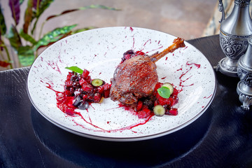 Fromt view on duck leg decorated with berry splashes and berries on white plate. Copy space. Meat food background. Close up. Duck confit. restsurant food