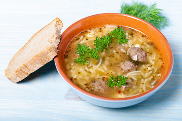 Homemade soup with noodles and meatballs on a wooden table. Traditional rural dinner