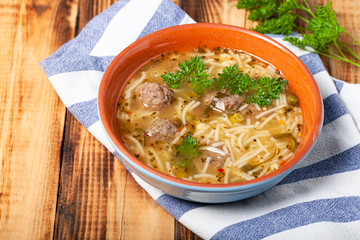 Homemade soup with noodles and meatballs on a wooden table. Traditional rural dinner