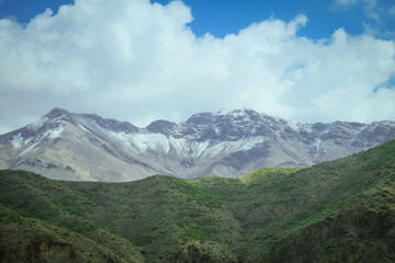 Landscape view of snow capped Atlas mountain range against cloudy blue sky, Morocco.